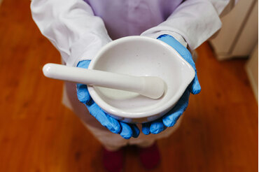 Gloved hands holding a white pestle and mortar
