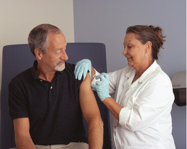 Man receiving an immunization from a woman in a white coat