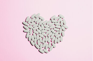 medication pills forming a heart against a pink background