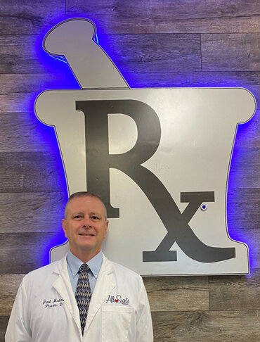 Paul Matar, Pharm D, in white coat in front of glowing Rx sign