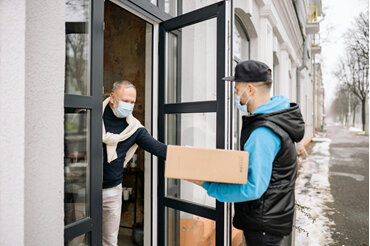 Person wearing a facemask receiving a delivery at their door